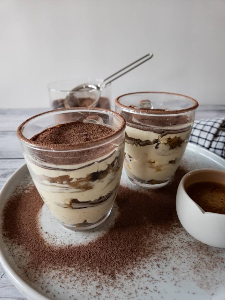 Klassisches Tiramisu im Glas mit Kakaopulver, serviert auf einem Teller